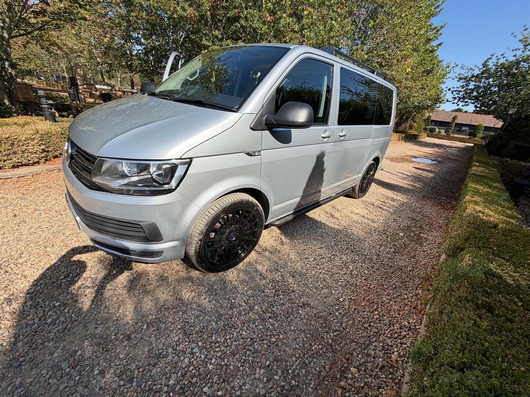 A silver Volkswagen Caravelle on the gravel drive at Rushgreen Farm, with the long brick outbuilding and trees behind